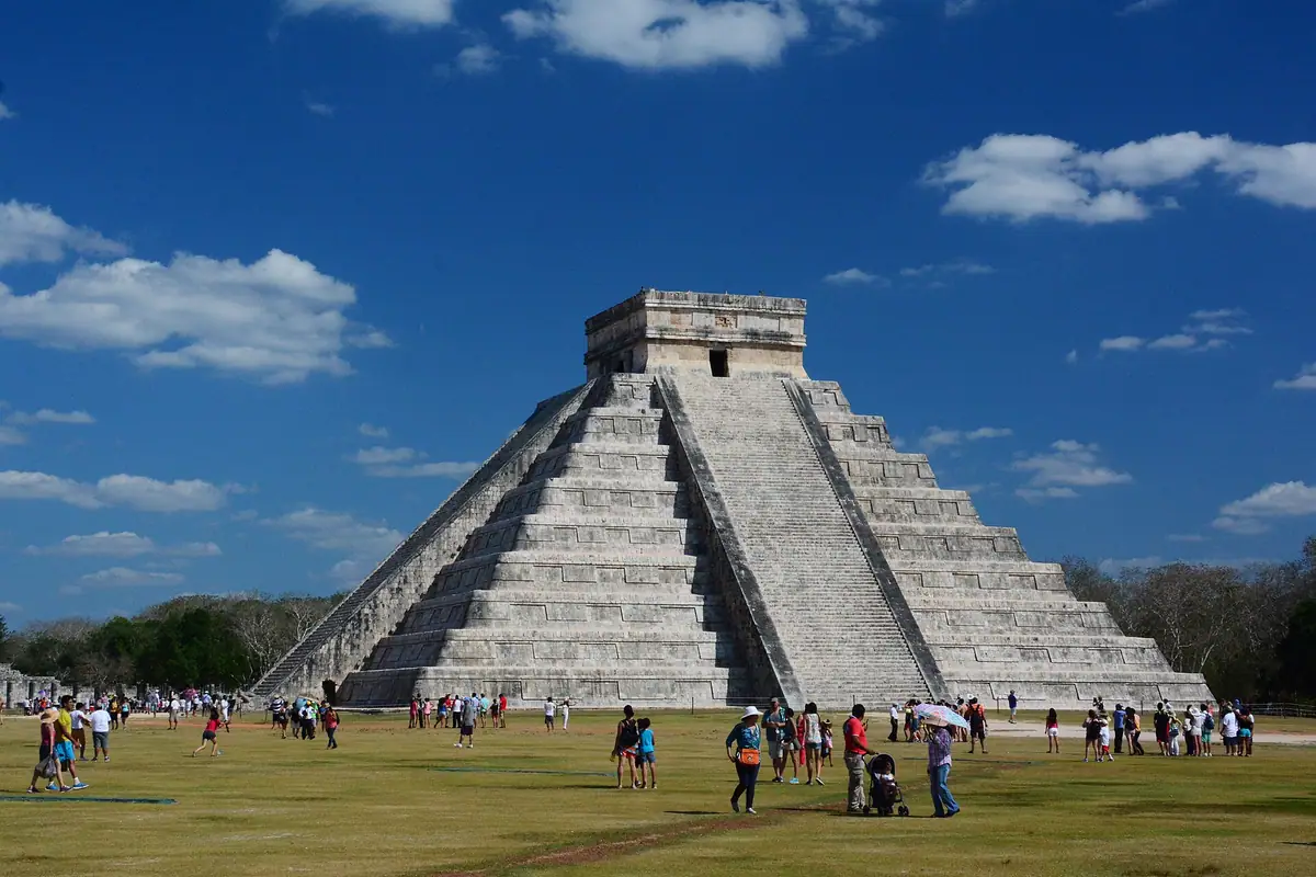Visitantes caminando por la explanada de piedra caliza frente a la pirámide de El Castillo en Chichén Itzá